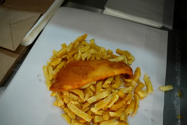 A whole battered cod fillet on a bed of thick-cut chips, wrapped open on paper at Ideal Fish & Chips