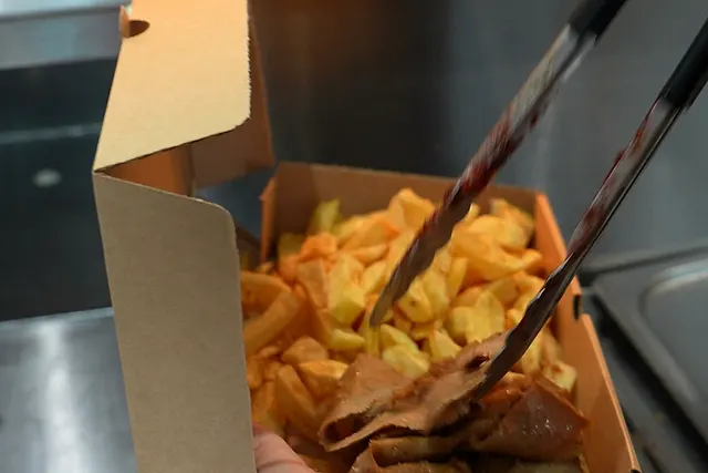 Carved kebab meat piled over thick-cut chips in a takeaway box