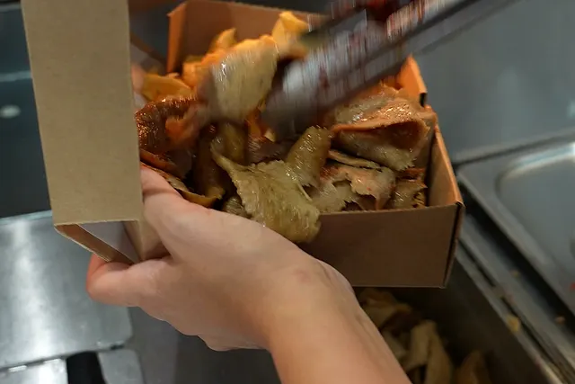 Freshly carved kebab meat being tonged into an open takeaway box