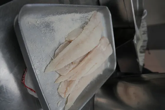 Fresh cod fillets dusted in flour, laid out in a tray ready for the batter