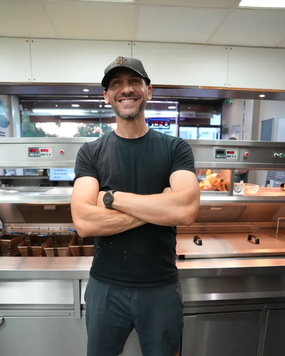 Terry Mouskos, owner of Ideal Fish & Chips, standing with his arms folded in front of the fryers in his Bromsgrove shop